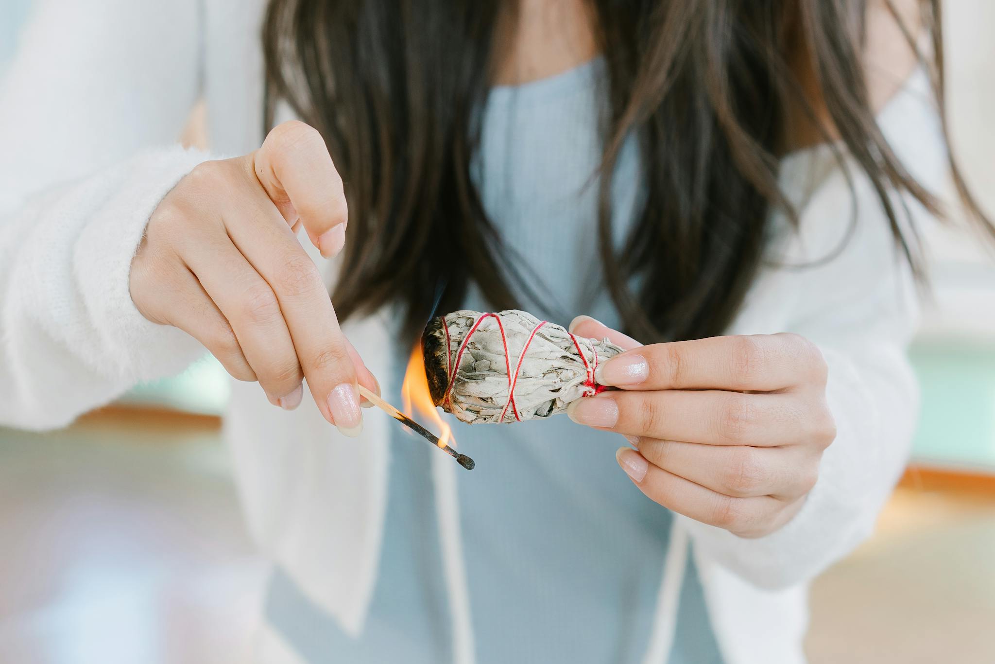A woman burning sage for a cleansing ritual indoors, promoting tranquility and spiritual healing.